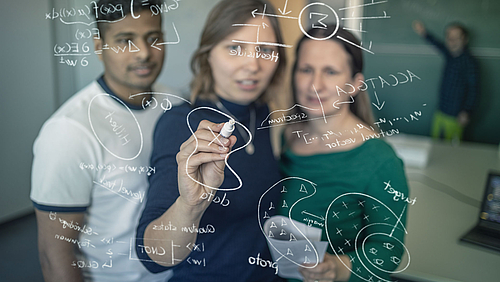 Forschung mit Sinn: Die Mittweidaer Mathematiker entwickeln nachvollziehbare KI-Werkzeuge. Zwei Frauen und ein Mann stehen vor einer Glasscheibe, auf die sie mathematische Formeln schreiben. Im Hintergrund steht ein Professor an einer klassischen Tafel.